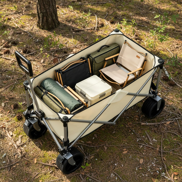 A silver and beige folding utility wagon with black wheels, shown loaded with camping gear including a folding chair, cooler, bags, and rolled gear on a clean white background.